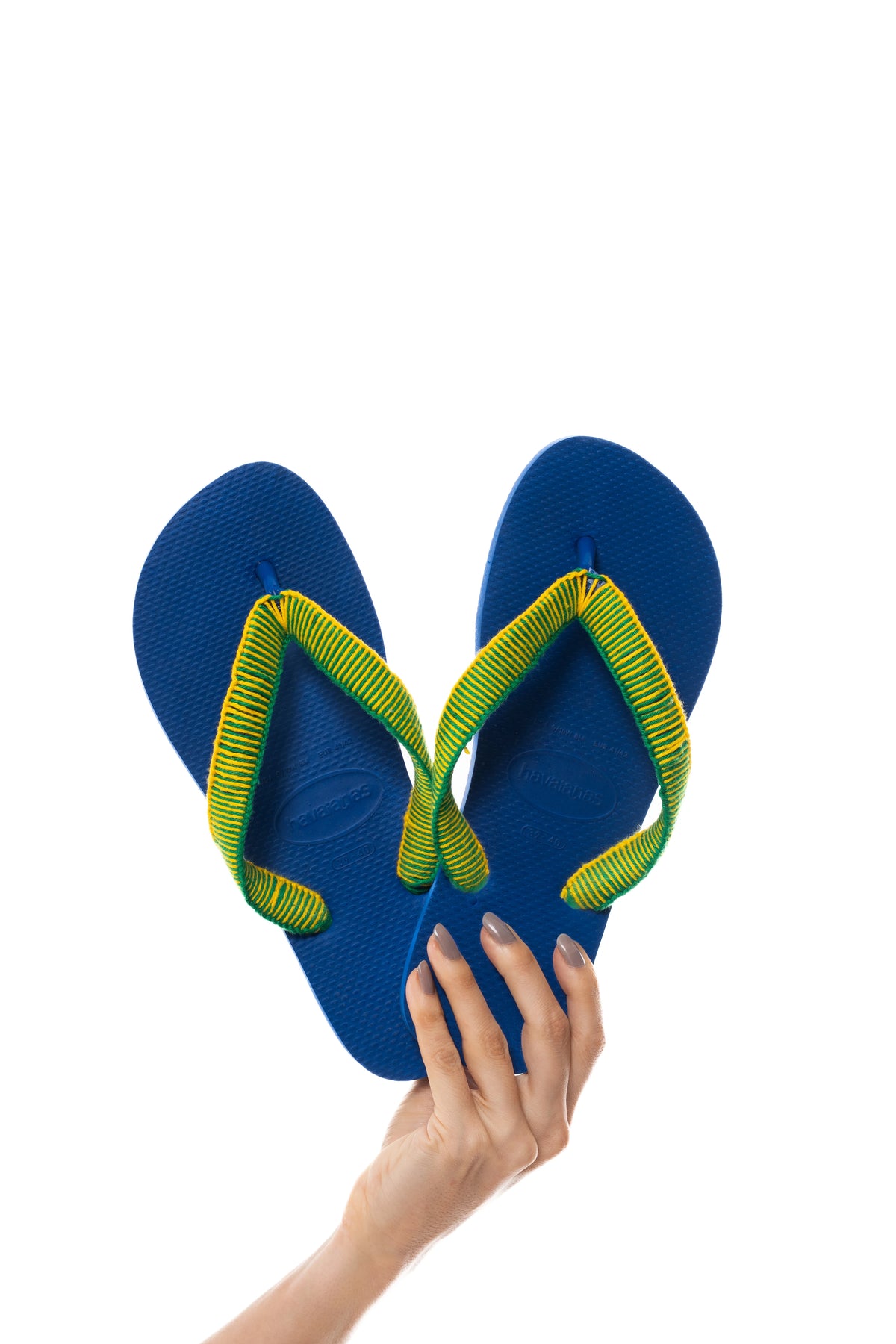 Havaianas Copa azul com tiras revestidas à mão em verde e amarelo, segurada na mão