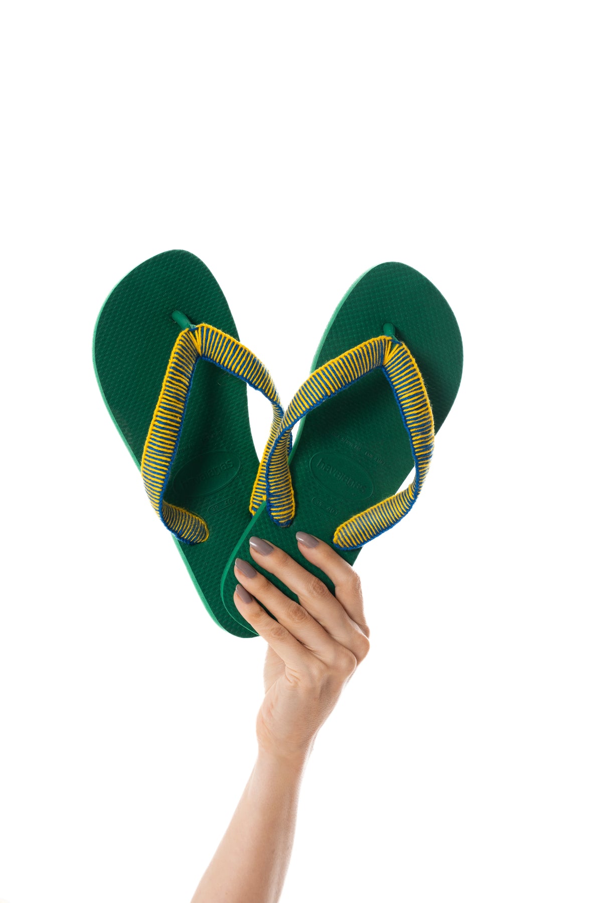 Havaianas Copa verde com tiras revestidas à mão em amarelo e azul, segurada na mão