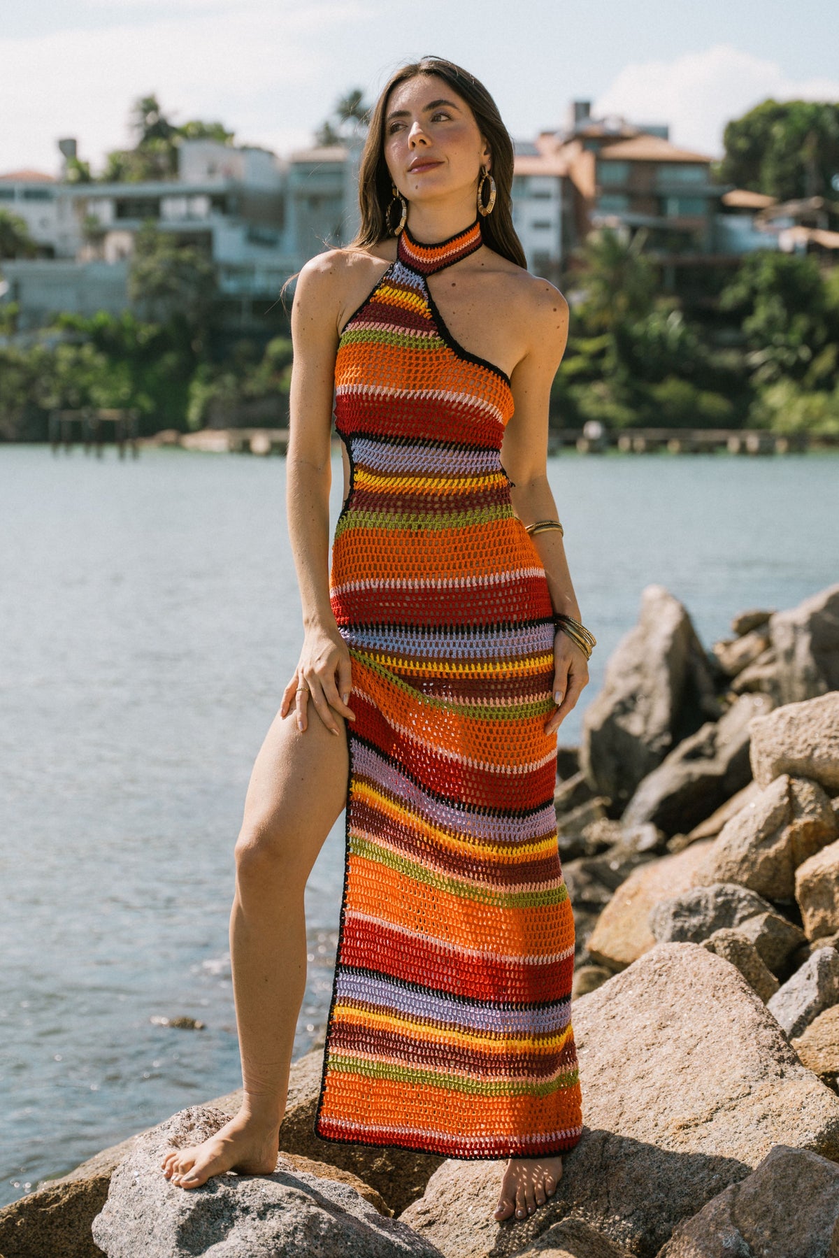 Modelo usa o Vestido Portofino de crochê listrado nas pedras à beira-mar